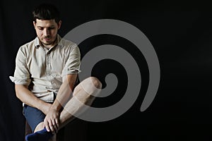 A young man is sitting on a stool and holding his leg with his hand. guy on a dark background in the Studio