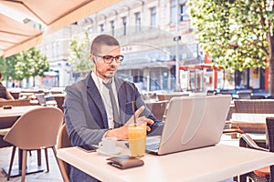 Young man sitting at  street cafe having a conversation on a laptop wearing a headphones