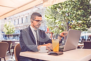 Young man sitting at street cafe having a conversation on a laptop wearing a headphones