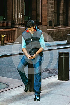 Young man sitting on street, texting on cell phone in New York City
