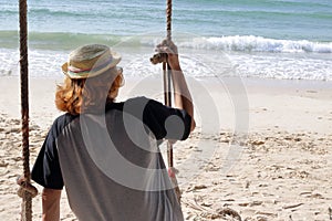 Young man sitting on the swing on the beach, feeling so sad ,alone,lonely