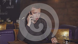 Young man sitting at a table in a cafe talking on the phone