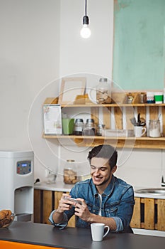 Young man sitting at a table in the kitchen with his mobile phone
