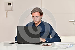 young man sitting on a table using a laptop next to some bills