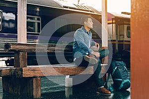 Young man sitting at train station with awaiting the train`s arr