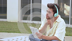 young man sitting on a university bench, watching tablet and listening to music