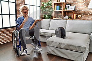 Young man sitting on wheelchair at for motorcycle accident amazed and smiling to the camera while presenting with hand and