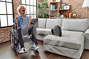 Young man sitting on wheelchair at for motorcycle accident celebrating mad and crazy for success with arms raised and closed eyes