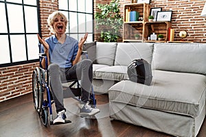 Young man sitting on wheelchair at for motorcycle accident celebrating victory with happy smile and winner expression with raised