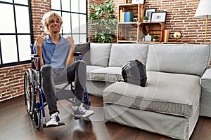 Young man sitting on wheelchair at for motorcycle accident looking confident with smile on face, pointing oneself with fingers