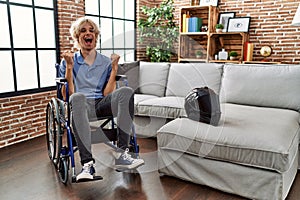 Young man sitting on wheelchair at for motorcycle accident screaming proud, celebrating victory and success very excited with