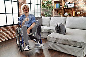 Young man sitting on wheelchair at for motorcycle accident smiling happy and positive, thumb up doing excellent and approval sign