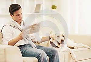 Young Man Sitting on White Sofa with Dog at Home.