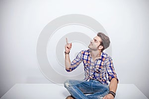 Young man sitting on a white table while pointing up