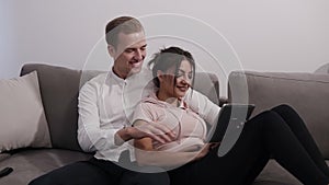 Young man sitting and woman in casual laying on a grey couch at home and looking at tablet. Spending their time together