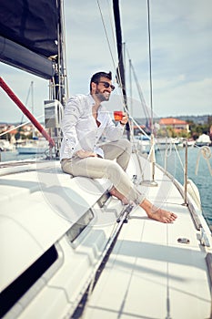 A young man sitting on a yacht and enjoying a coffe and a view on the dock. Summer, sea, vacation