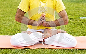 Young man sitting in yoga pose at green grass in the meadow and meditates. Muscular guy relaxing in lotus pose.