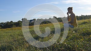 Young man sitting in yoga pose at green grass in the meadow and meditates. Muscular guy relaxing in lotus pose at nature