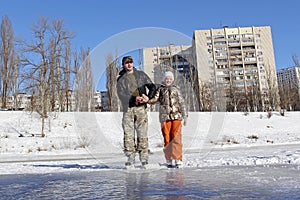 A young man on skates holds a little girl on skates on a ice skating rink in winter day