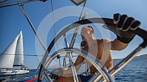 Young man skipper steering wheel during sea yacht race.