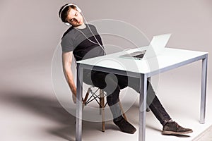 Young man sleep while wearing headphones and work on laptop on his office table on white background. work