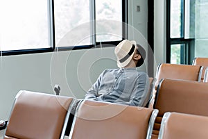 Young man sleeping alone in airport waiting area, relaxing on chair with hat covering face, resting during layover or travel delay photo