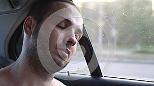 Young man sleeping inside moving car during long journey. Portrait of tired passenger traveling by car at summer evening