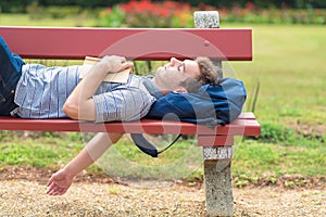 Young man sleeping in the park with a book