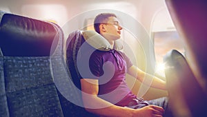 Young man sleeping in plane with travel pillow