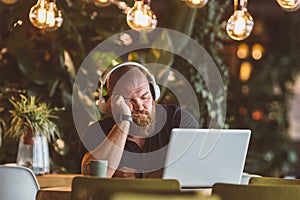 A young man sleeps fell asleep at the table with headphones in front of the computer in the restaurant
