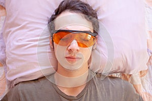 Young man sleeps while wearing red sleep glasses with blue light filtering lenses