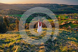 A young man in a Slovak folk costume looks at the spring landscape in the village of Hrinova in Slovakia. Rising sun and spring