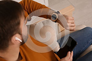 Young man with smart watch, phone and earphones at home, above view