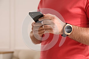 Young man with smart watch and phone at home, closeup. Space for text