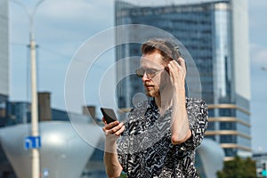 A young man with a smartphone in headphones and sunglasses