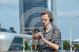 A young man with a smartphone in headphones and sunglasses
