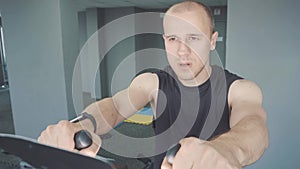 Young man with smartwatch riding stationary bike in gym
