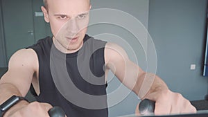 Young man with smartwatch riding stationary bike in gym