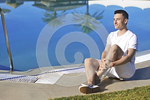 Young man smile in white clothes, posing near pool beackground palms. Man burns, relaxes, rests, travels. Sunbathing