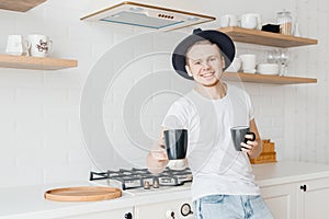 Young man smiles and shares freshly prepared coffee in ceramic black mug. Bright kitchen background