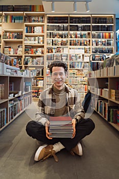 Young man smiling with books in modern library interior