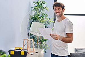 Young man smiling confident repairing lamp reading instructions at home