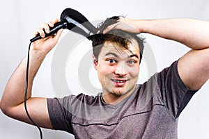 Young man smiling while he dries his hair. Teenager holding hair electric fan. Young man dries hair with an electric fan. Preparin