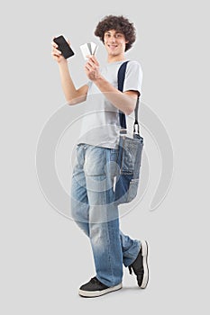 young man smiling and handsome showing mobile phone and credit card dressed in jeans and t-shirt with shoulder bag, isolated on