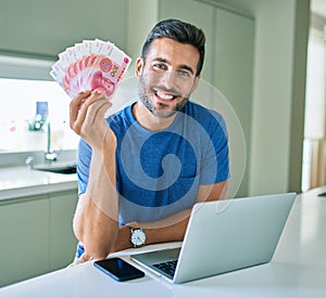 Young man smiling happy holding chinese yuan banknotes at home