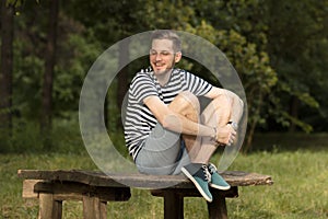 Young man smiling laughing sitting on wood table in nature fores