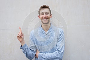 Young man smiling and pointing finger up against blank wall