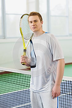 Young man smiling and posing with tennis racket indoor