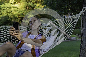 Young man smiling taking a selfie for their friends while sitting in a hammock in summer vacation time