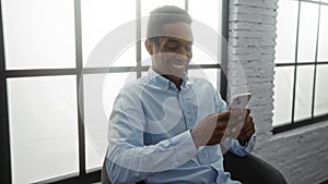 Young man smiling while using smartphone indoors at workplace showcasing technology-driven environment photo